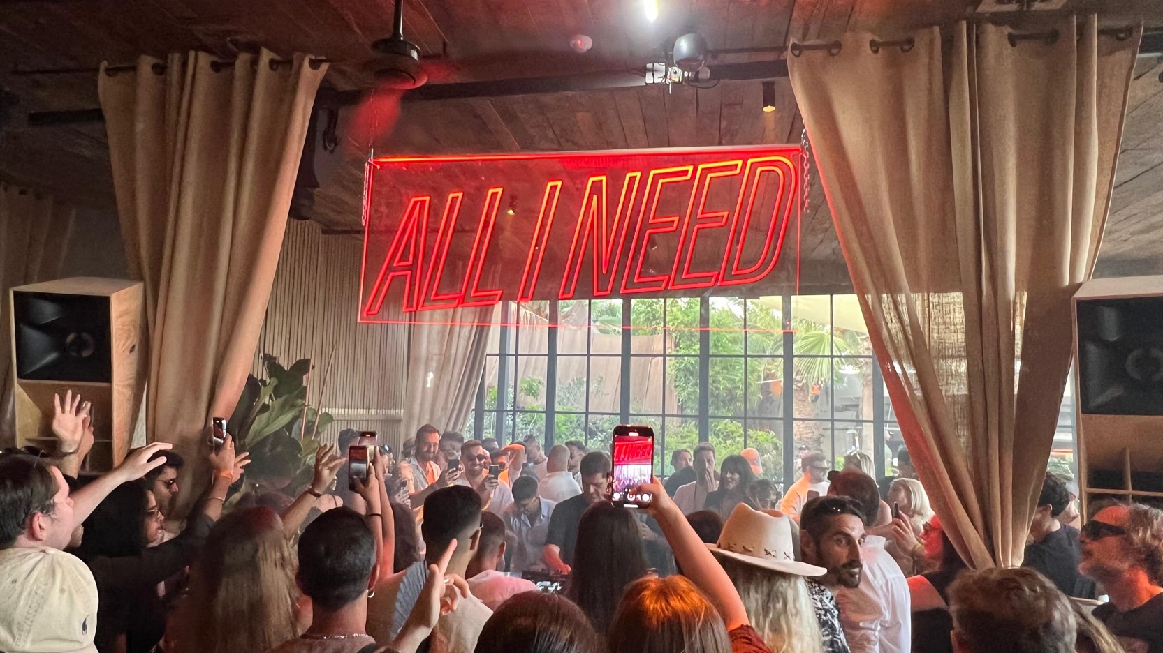 ALL I NEED neon sign above a full dancefloor